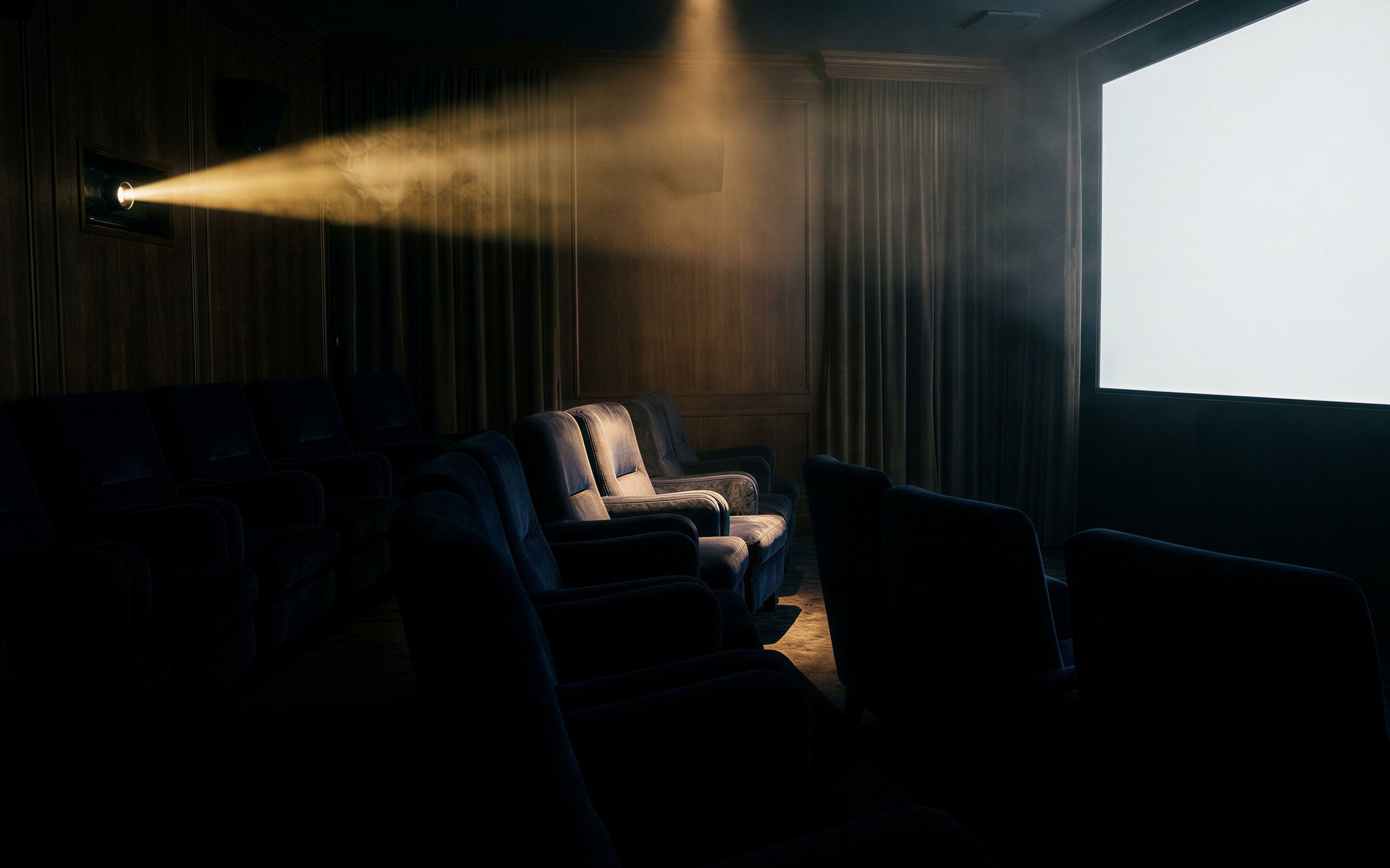 An empty screening room: a projector beam through haze toward a blank screen